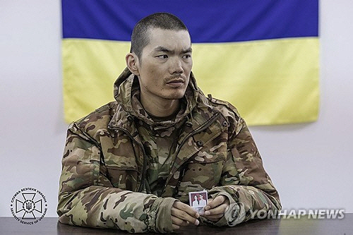 9일(현지시간) 우크라이나군에 생포된 중국인 남성이 우크라이나 당국에 심문을 받으면서 가족 사진을 보여주고 있다.  [우크라이나 보안 당국 제공=키이우 EPA 연합뉴스]